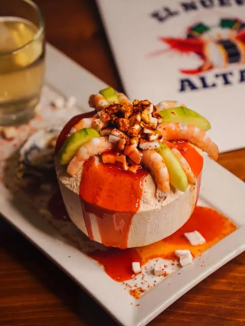 Un coco fresco con camarón, aguacate y chamoy, con el menú de El Nuevo Altata al fondo.