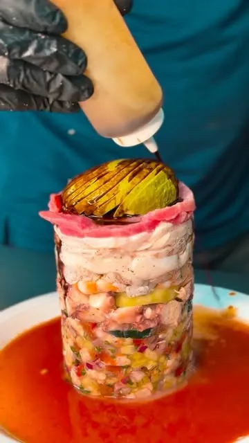 Una torre alta de mariscos en capas con aguacate rebanado encima, bañándose en salsa.